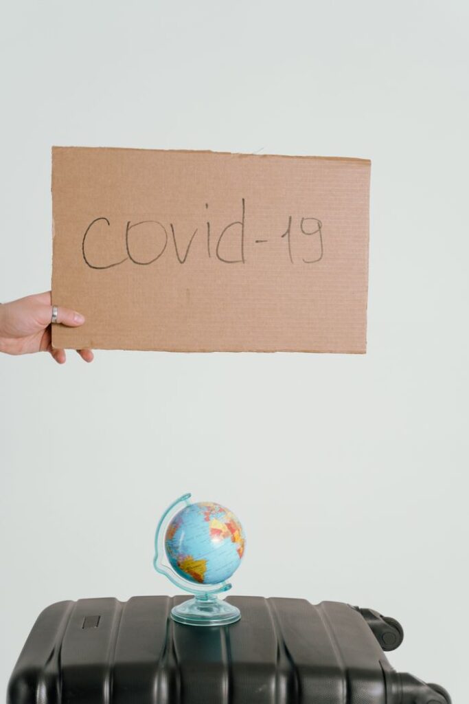 Conceptual image of a cardboard COVID-19 sign held above a mini globe on a suitcase.